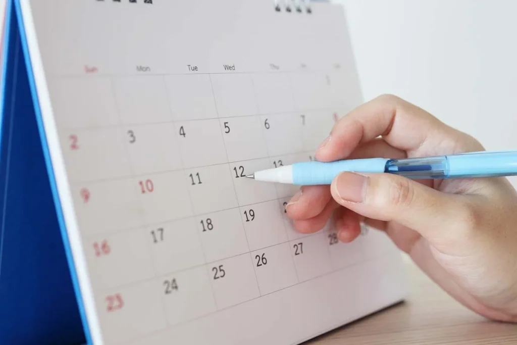 A hand using a pen to encircle a date on a clean paper wall calendar