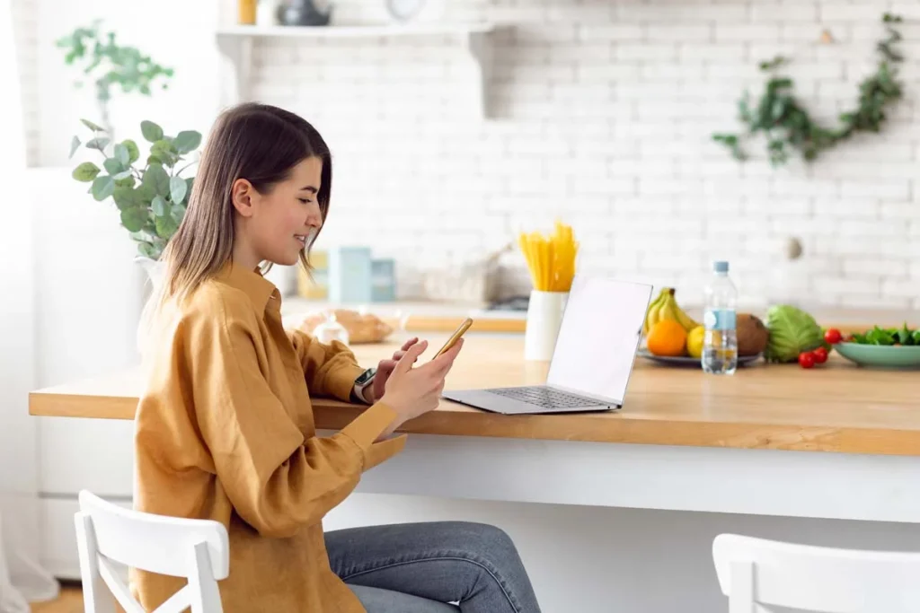 A person sitting at a bright kitchen table using a laptop to fill out an online form