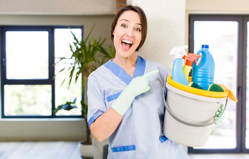 A smiling, looking excited professional cleaner holding a bucket of cleaning supplies ready for cleaning services