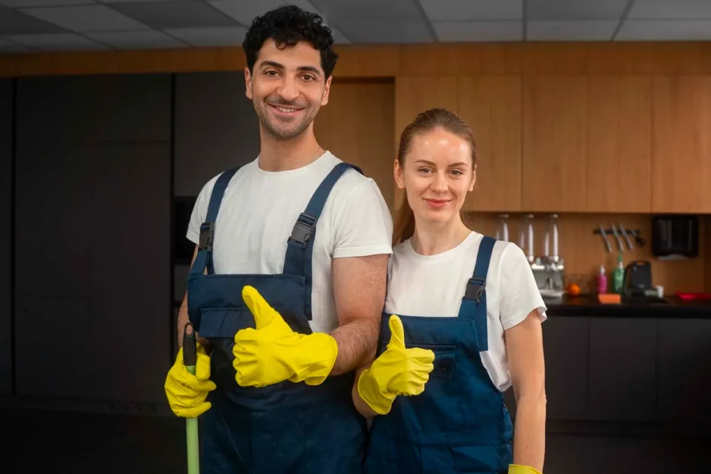 Two friendly professional cleaners in uniforms ready to clean the office