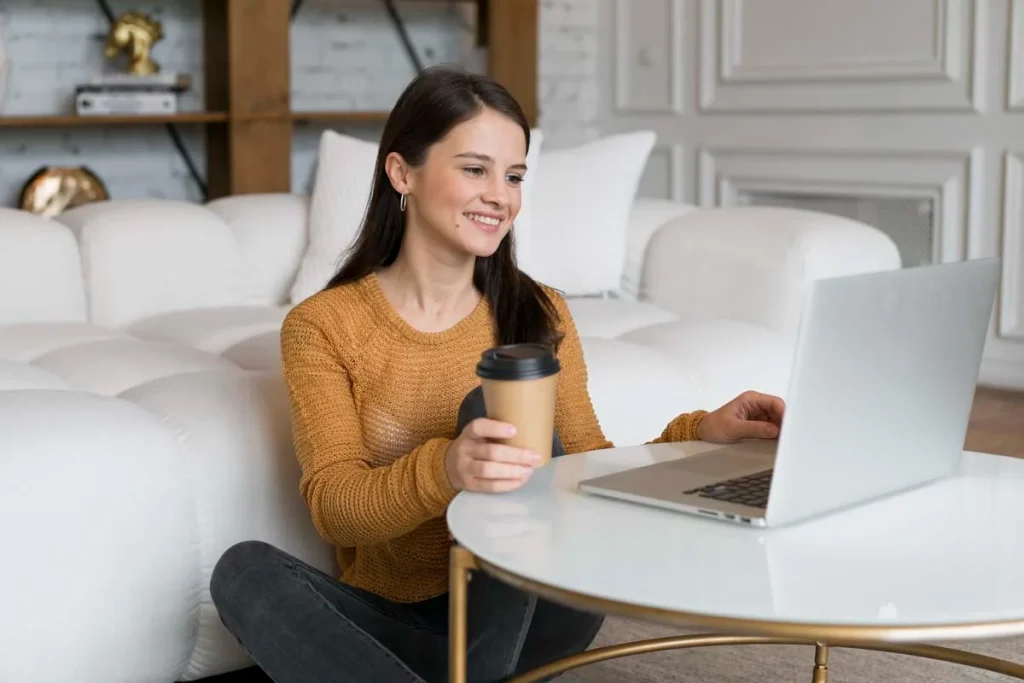 Happy woman smiling at her laptop in a modern condo while requesting a free cleaning quote online